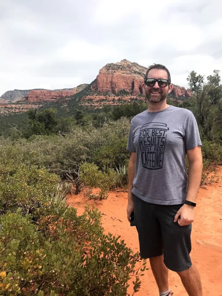 Ryan Lowe on a hiking trail with red rock cliffs behind him